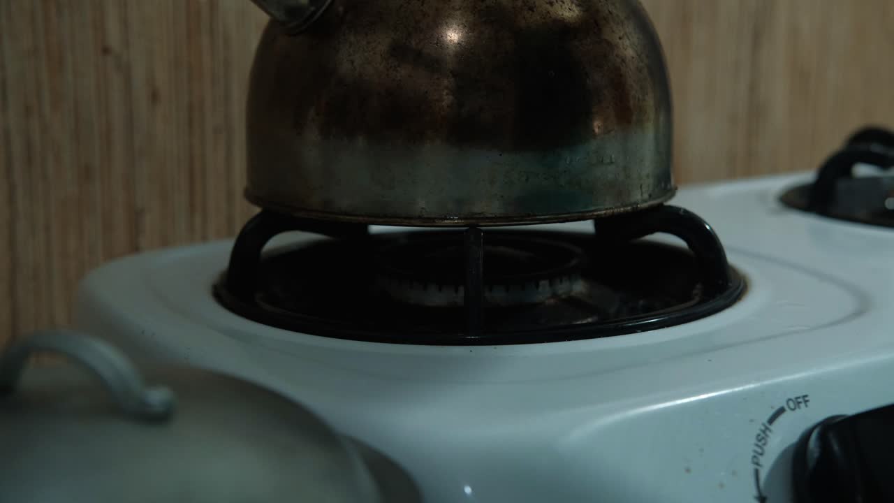 Static shot of a stovetop kettle being placed on stovetop as the burner turns on.