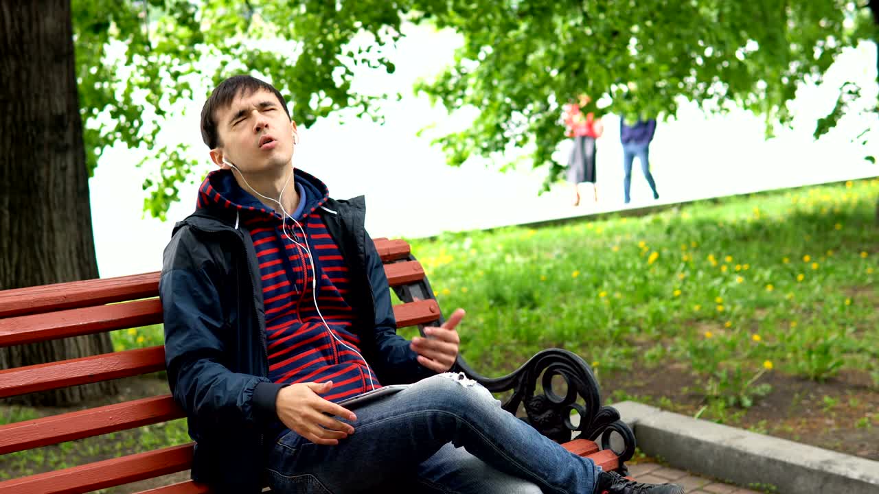 한 남자가 공원에서 음악을 듣고 태블릿을 사용하고 있습니다.