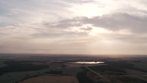 aerial view of a tranquil lake at sunset with sprawling fields under a cloudy sky