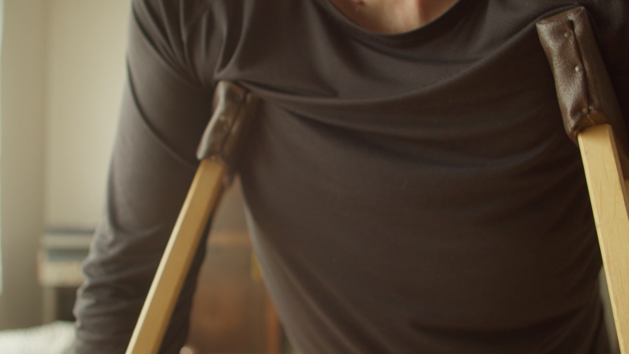 Medium shot of a man utilizing wooden crutches under his arms to maintain balance. Ideal for disability representation, healthcare services, and orthopedic equipment ads.