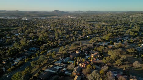 drone arcs around rivett revealing neighboring suburbs, classic homes, trees, and hills lit by the setting sun