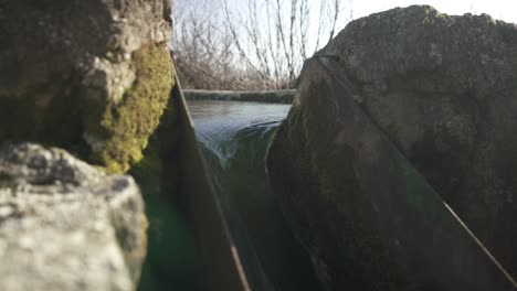 Water-falling-into-canal-between-rocks-covered-by-moss,-dranage-concept