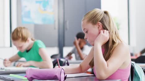 diverse schoolchildren writing and sitting at desks in school classroom