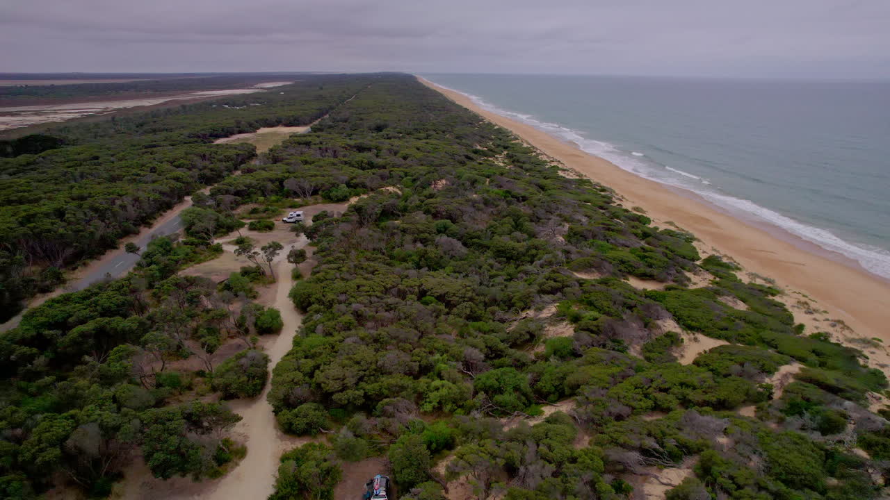 Aerial shot rising over remote campsite at 90 Mile Beach in Victoria, revealing endless sandy beach, dunes, and lush green vegetation along the wild coastline