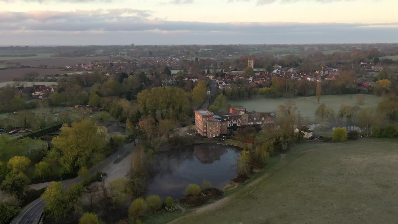 An aerial flight over Dedham Mill towards Dedham village at sunrise with low mist.