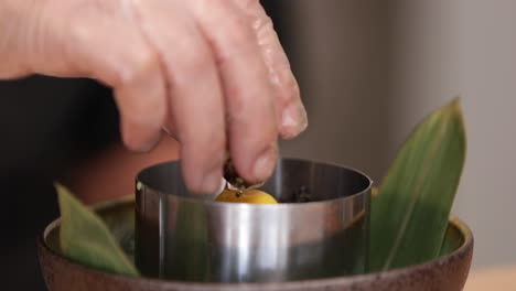 sushi chef putting quail egg yolk and shell on top of tuna tartare inside the stainless moulder