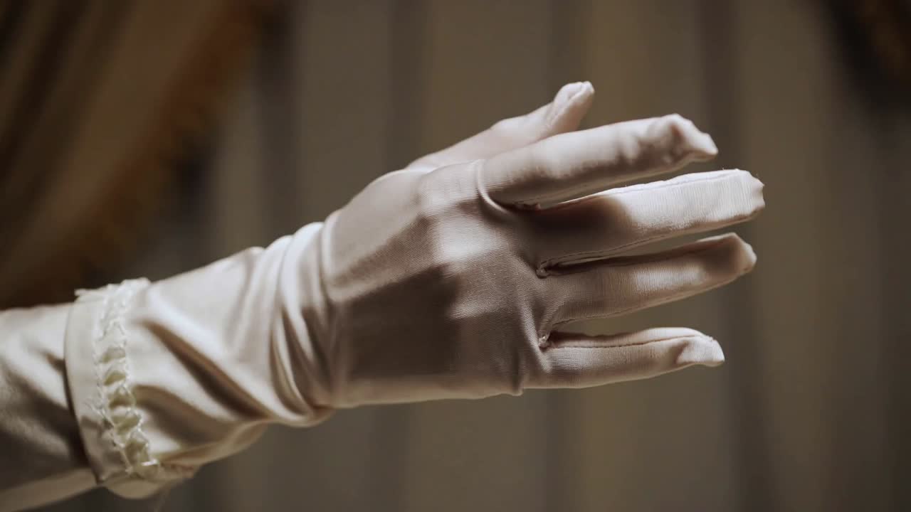 Entering gloved right hand rotating wrist, spreading fingers at curtain, showing ruffled cuff seams