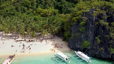 Playa-De-Los-Siete-Comandos-En-El-Nido-Con-Turistas-Nadando-En-Aguas-Cristalinas-De-Color-Turquesa-Y-Barcos-Turísticos-De-Isla-En-Isla