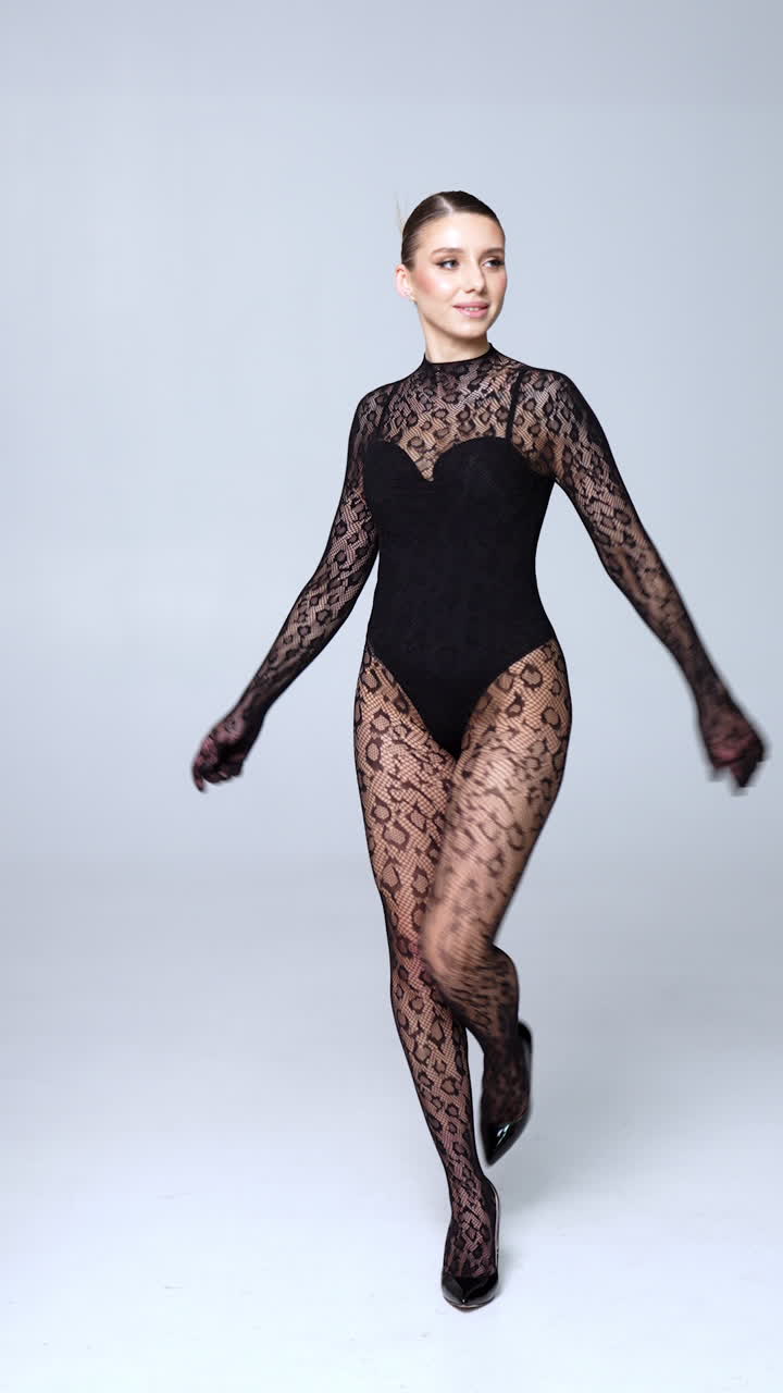 Beautiful Caucasian woman wearing black bodysuit and long-sleeve lace outfit in studio. Model walks on high heels. Vertical video.