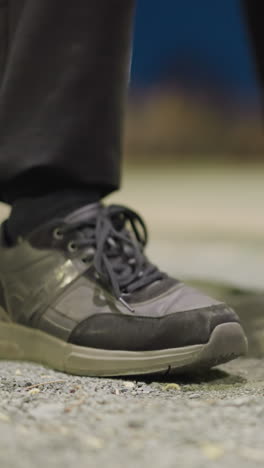 primer plano de los pies de una persona mientras golpean repetidamente el suelo, con un fondo borroso y débilmente iluminado y una barandilla de hierro visible en la distancia