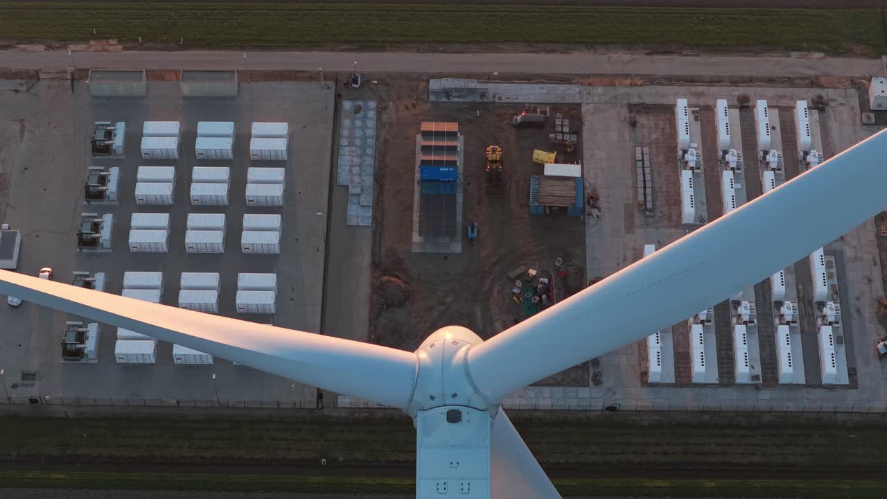 Wind turbine blades spinning above a battery storage system