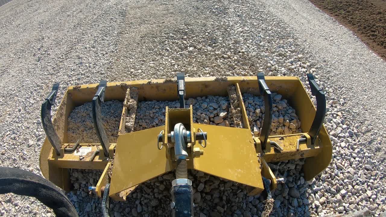 새로운 자갈이 깔린 차도를 평평하게 하기 위해 상자 스크래퍼가 떨어지고 상자에 자갈이 모입니다.