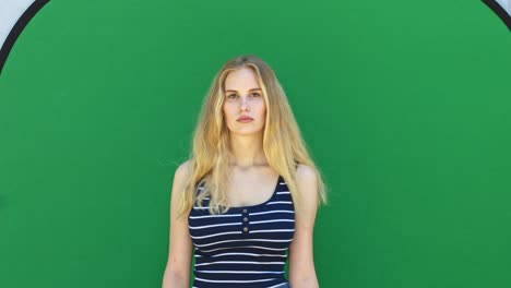 static medium shot of a blonde lady model posing in front of a chroma key with a blank facial expression