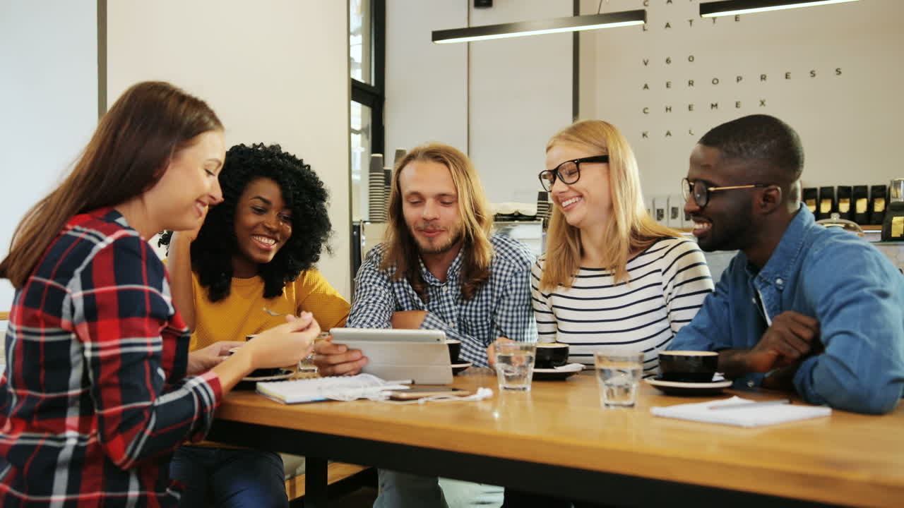 Group multiethnic group of happy friends talking and drinking coffee sitting at a table in a cafe