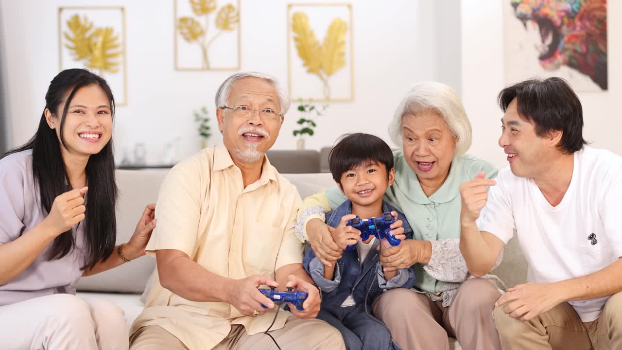 明るく居心地の良いリビングルームで、3世代のアジア人家族が楽しそうにビデオゲームをしています。