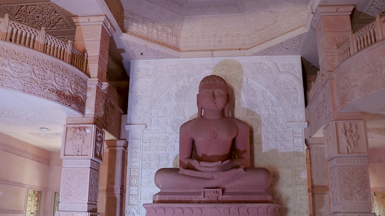 estatua sagrada de piedra roja aislada de dios jainista en meditación desde diferentes ángulos el video se tomó en shri digamber jain gyanoday tirth kshetra, nareli jain mandir, ajmer, rajasthan, india