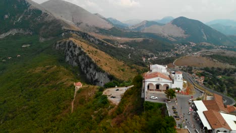 AERIAL-DOLLY-IN:-drone-flying-towards-a-typical-small-Italian-church-in-an-extreme-setup-on-top-of-an-isolated-hill-surrounded-by-an-incredible-view-of-mountains-in-south-of-Italy,-Maratea-Basilicata