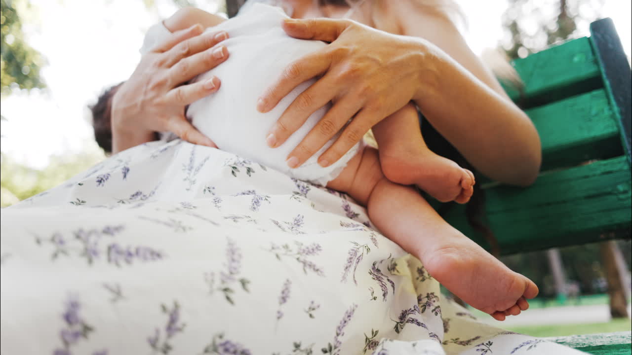 Tender moment of a mother breastfeeding her baby on a green park bench in daylight