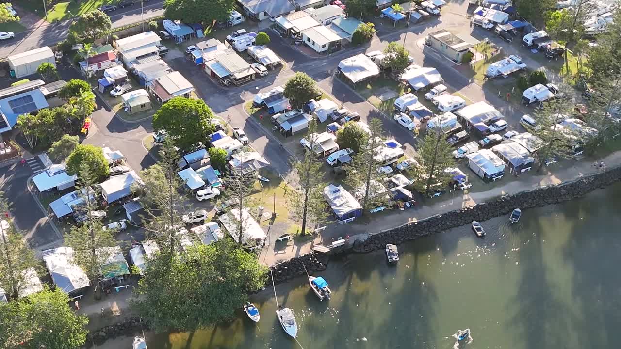 Aerial perspective of a riverside caravan park with boats and lush greenery.