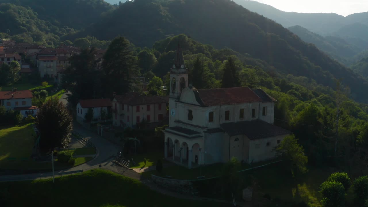 Veduta aerea della suggestiva chiesa parrocchiale di un villaggio italiano situata accanto a colline boscose ad Arola, Italia