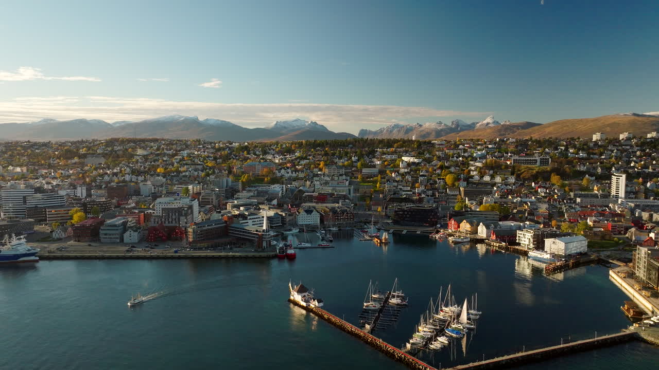 Aerial view over Tromso harbor with docked boats and snowy mountain peaks