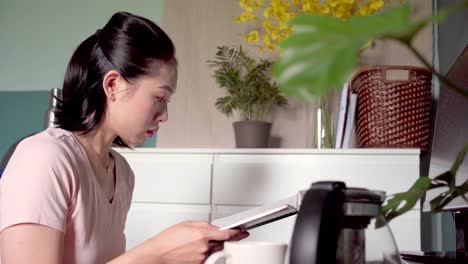 asian woman reading notes in notepad and working from home