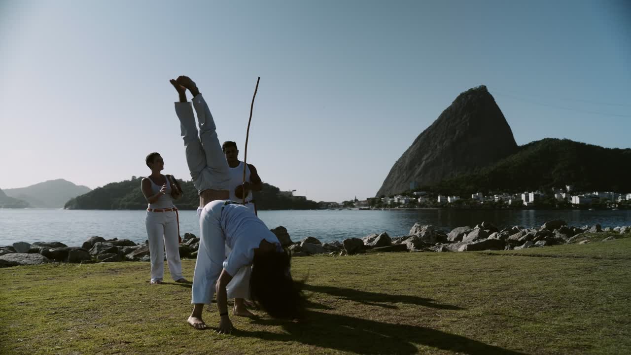 People practicing Capoeira outdoors with Sugarloaf Mountain in Rio de Janeiro