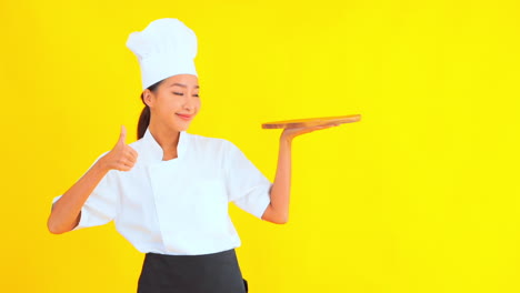 mujer asiática con sombrero de chef sosteniendo una tabla de cortar de madera