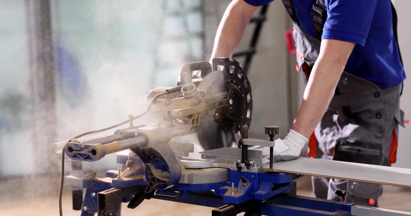 Un operaio prende una tavola di legno tagliata con una sega a disco in una casa ristrutturata.