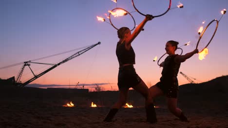 professional artists show a fire show at a summer festival on the sand in slow motion. fourth person acrobats from circus work with fire at night on the beach.