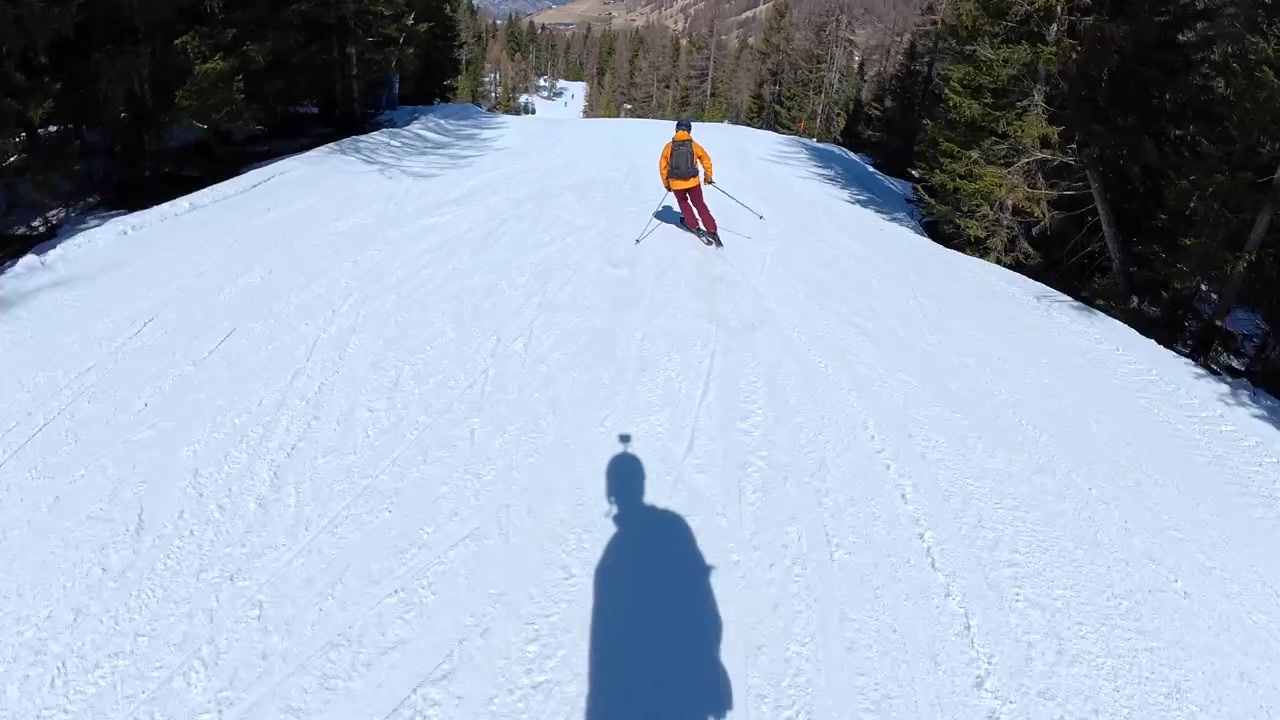 Sciatore che scende un pendio di montagna soleggiato.