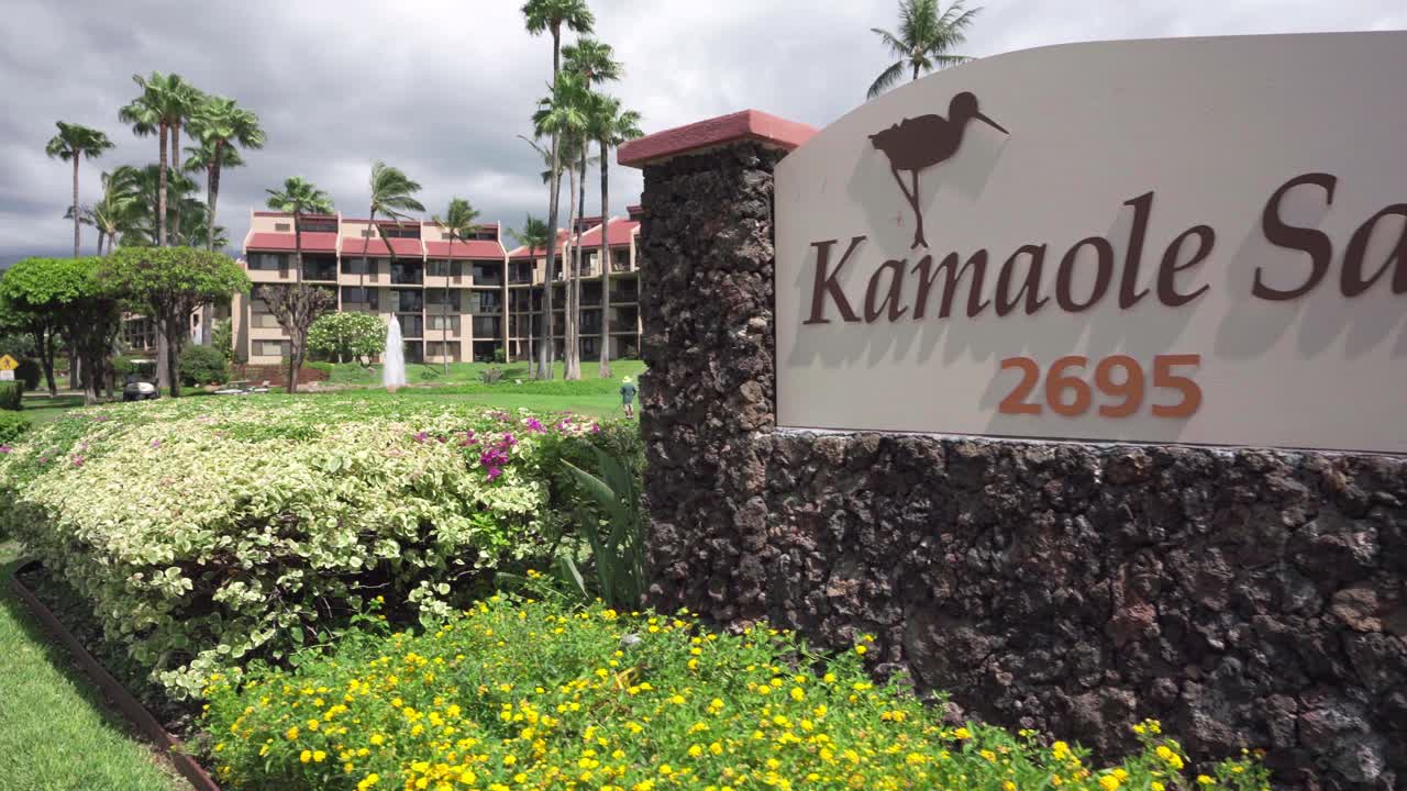 Touristic resort KAMOLE SANDS in Hawaii welcoming tourists on apartments with ocean view, surrounded by green grassland, view from the main gate