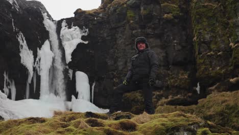 puesto turístico masculino en el área de turismo cerca de la cascada y el escuro acantilado volcánico
