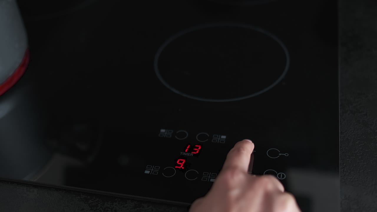 Donna preme un tasto per regolare il piano cottura a induzione nero in cucina