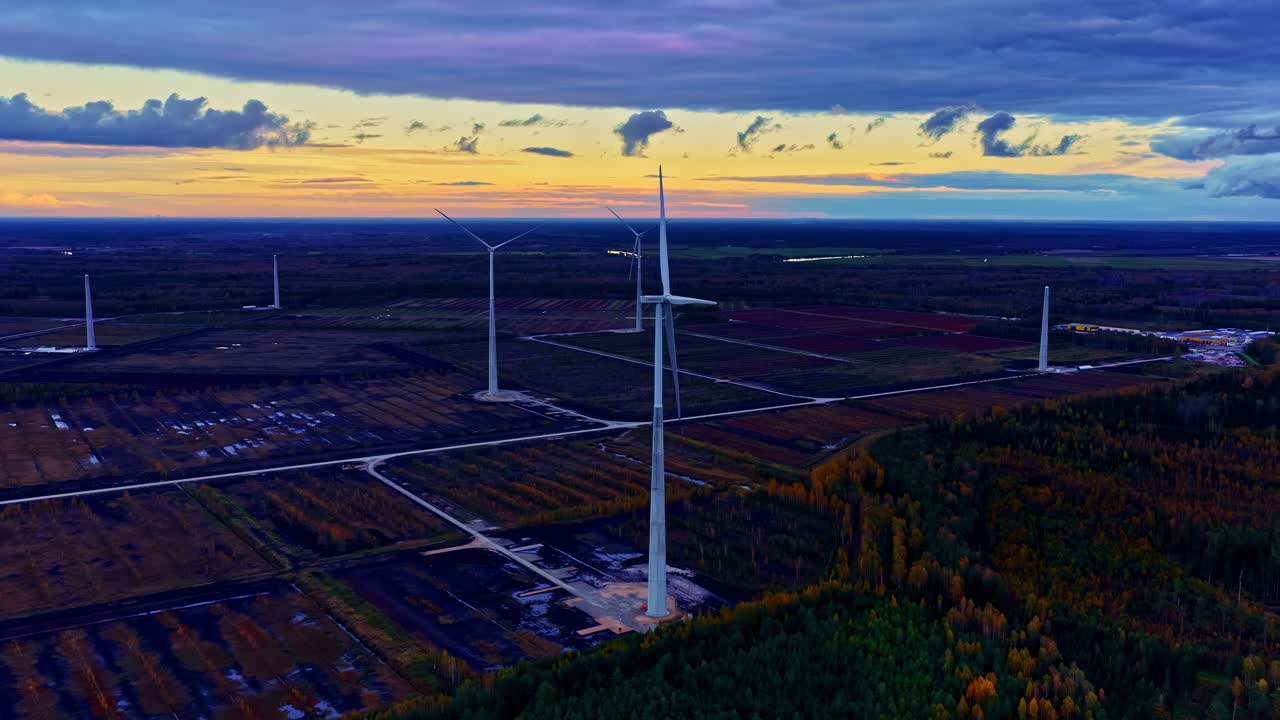 Luftfoto ved solnedgang af infrastruktur for vedvarende vindenergi med skovlandskab.
