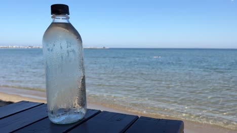 Primer-Plano-De-Una-Botella-De-Agua-Fría-De-Condensación-Con-El-Telón-De-Fondo-Del-Mar-Griego