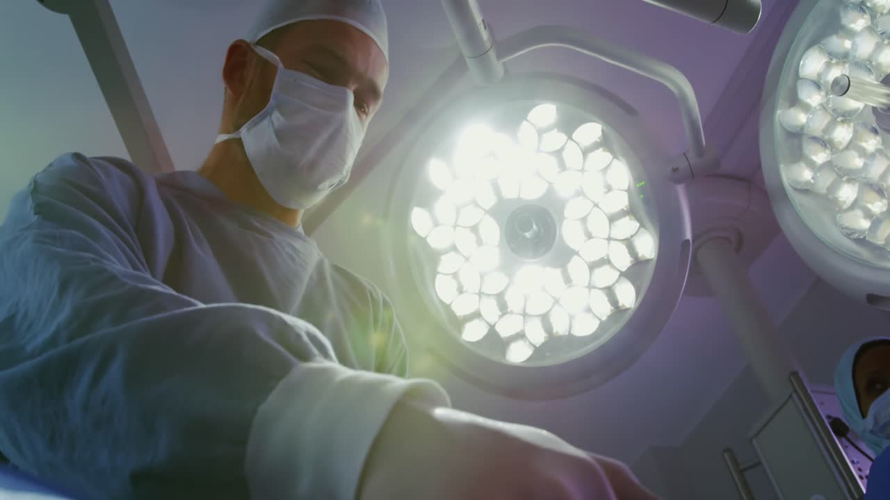 vista a basso angolo di un chirurgo caucasico che usa il defibrillatore su un paziente in sala operatoria in ospedale