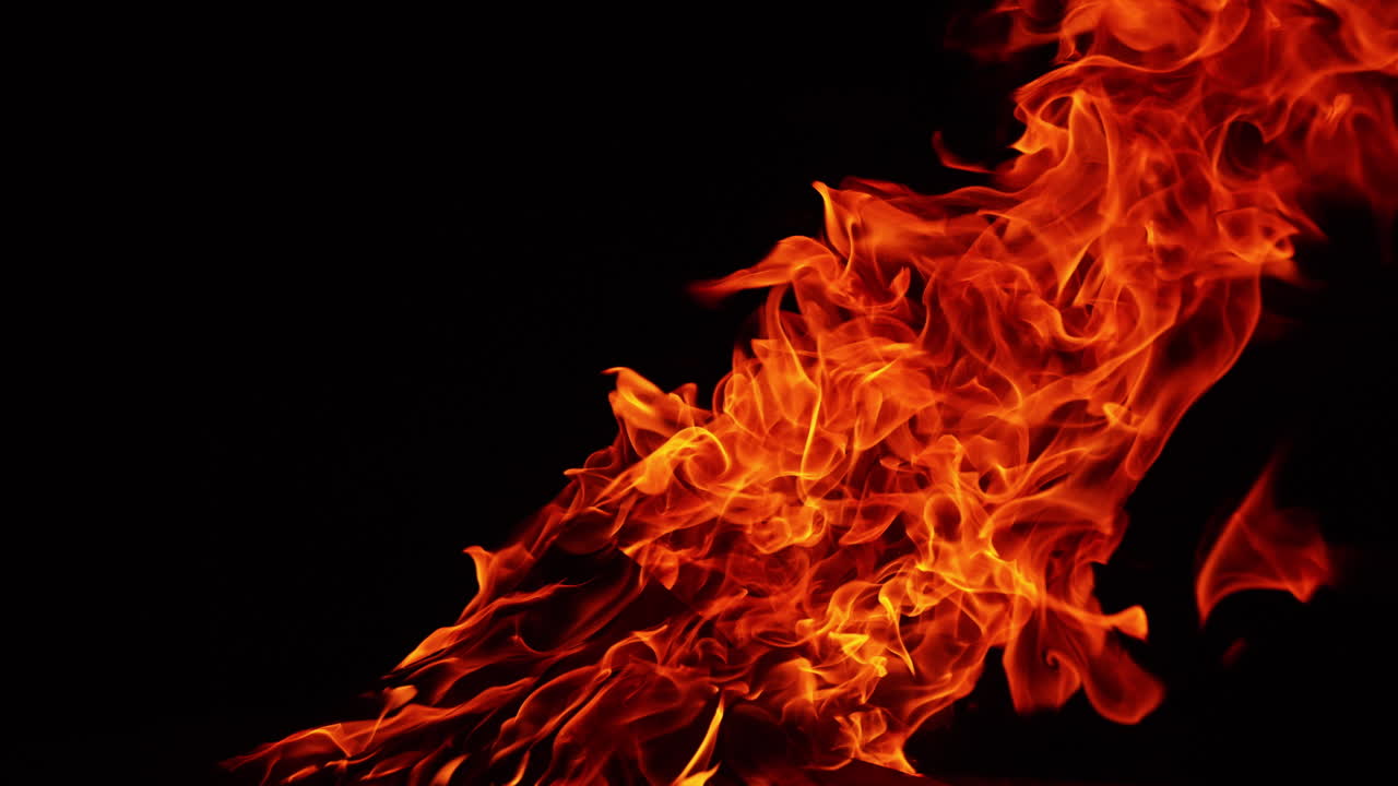 A long flame of bonfire stretching to the side from the wind. Isolated campfire at black backdrop.