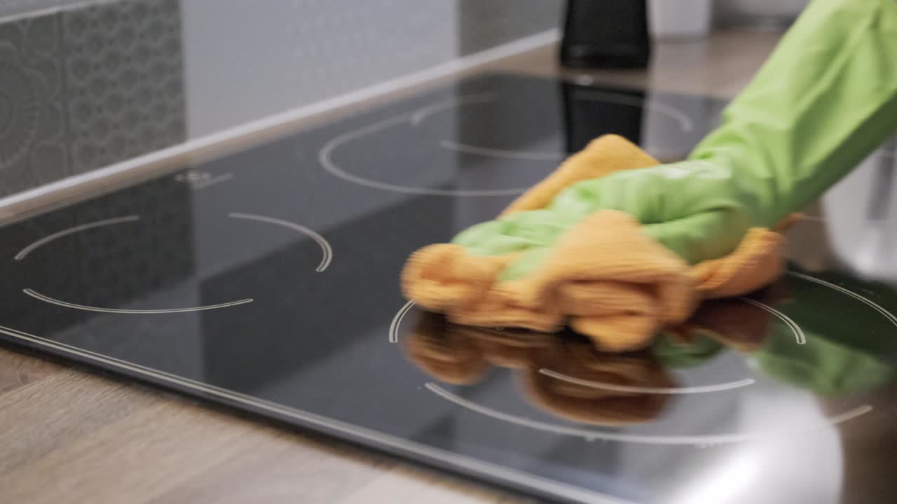 Primo piano della mano di una donna che pulisce un moderno piano cottura elettrico in vetroceramica con uno straccio