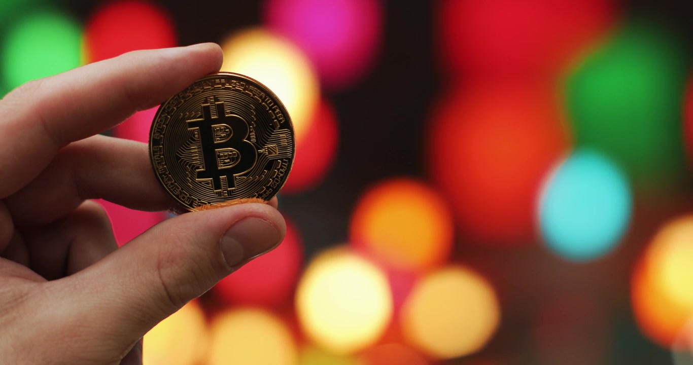 Mano sosteniendo moneda de Bitcoin dorada con fondo bokeh colorido