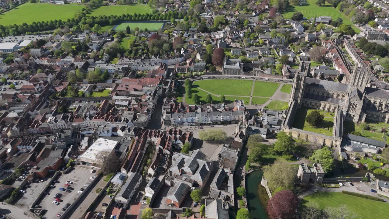 Aerial orbit of medieval cathedral city with towering Gothic spires above orderly stone rooftops, lawns and lanes portraying a preserved cultural heart