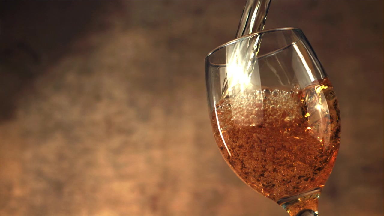 Liquido dorato versato in un calice da vino al rallentatore