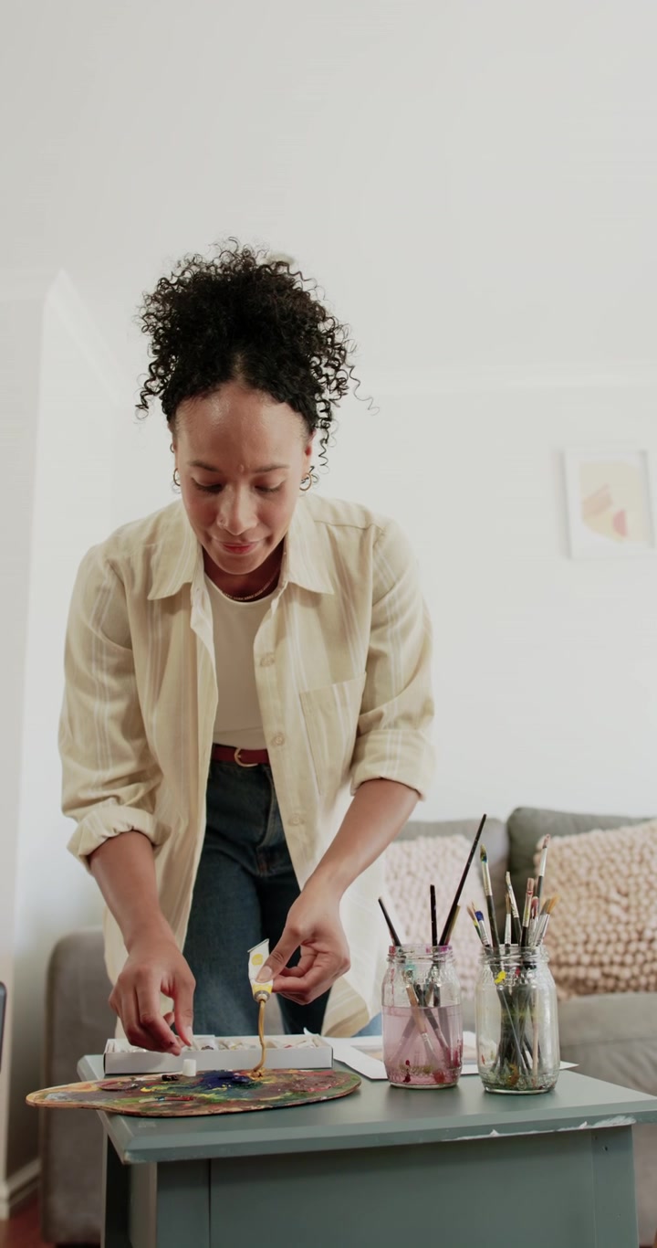 Vertical video: Adult woman leaning over table at home, preparing paints on palette for painting