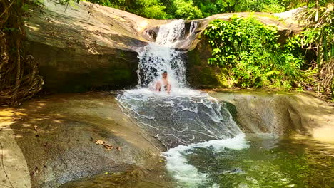 a shot of a happy man sliding and playing by the water falls