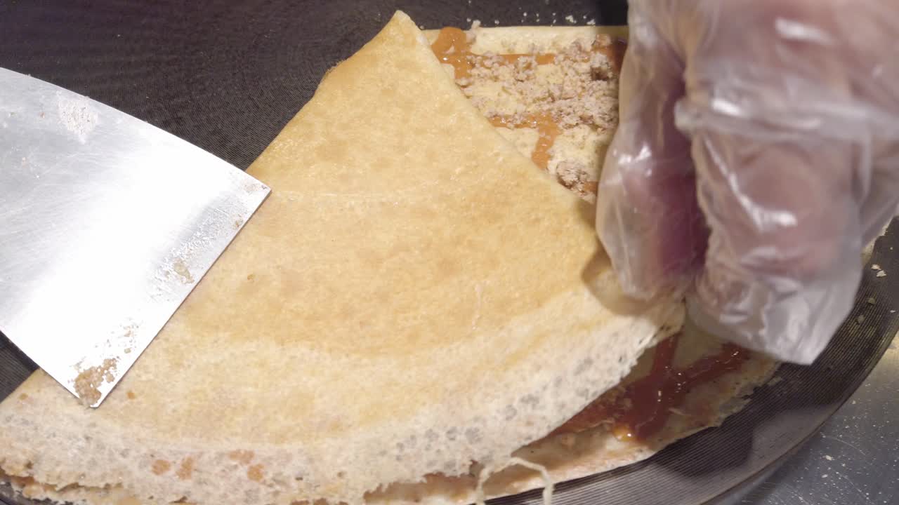 Pan shot of cook's hand folding a pancake with caramel on it, handheld shot