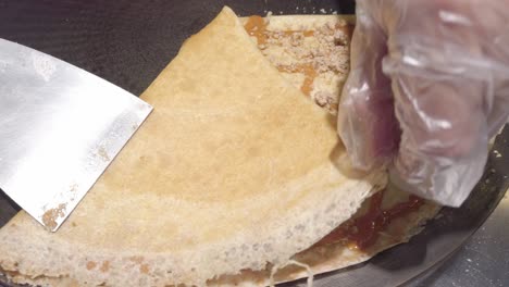 pan shot of cook's hand folding a pancake with caramel on it, handheld shot