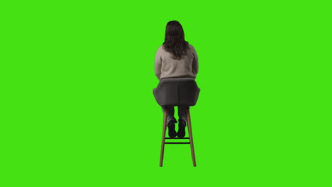 뒷면 전체 길이 은 캐주얼 옷을 입은 젊은 여성이 의자에 앉아 녹색 화면을 기다리고 있습니다.