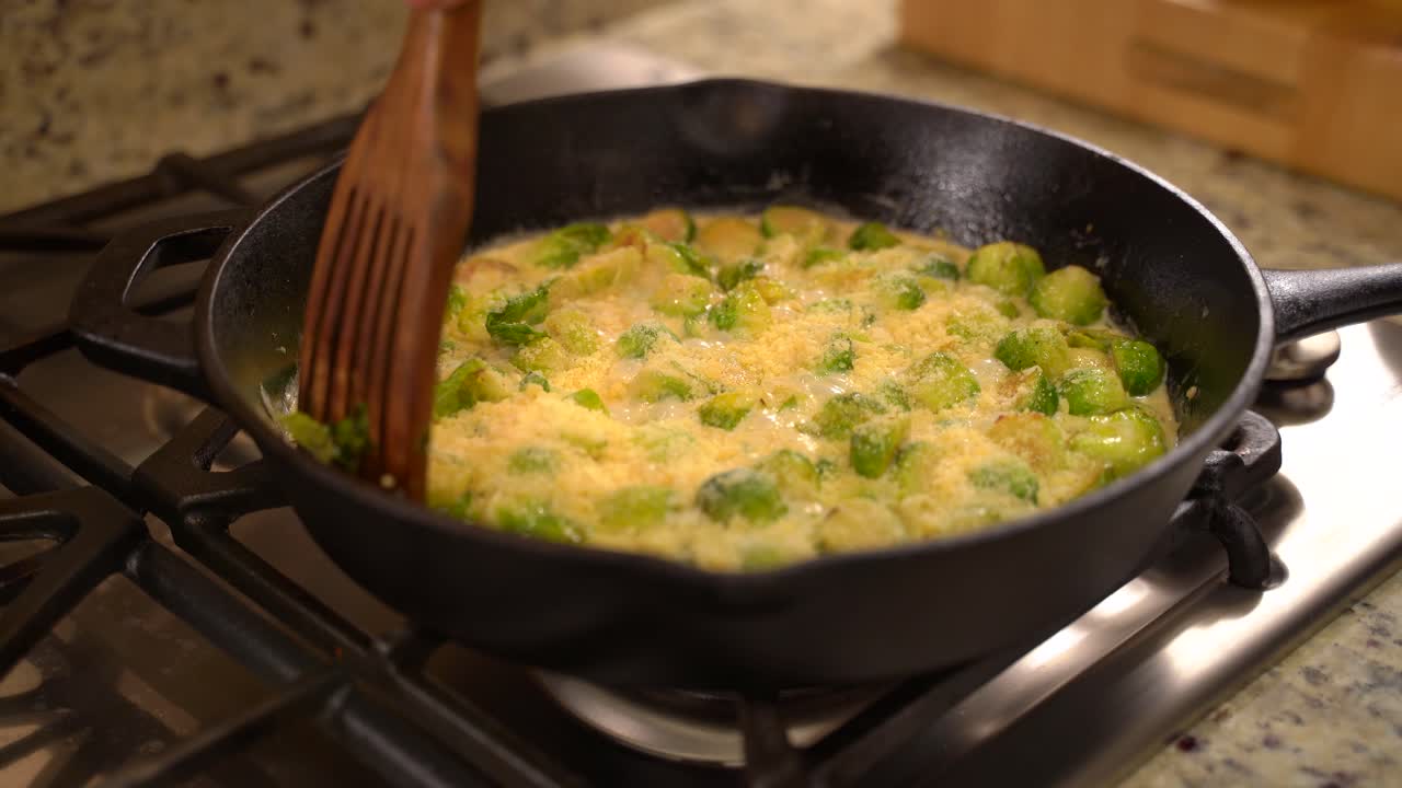 Cooking Roasted Sautéed Brussels Sprouts in a Cast Iron Pan Skillet - Stirring in Parmesan with a Wooden Spatula