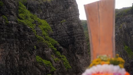 hugely steep mountain sides that have barely grown in wang long bay where a traditional thai boat sails slowly into the bay