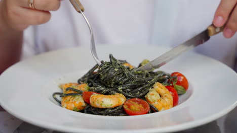 person eating black pasta with shrimp and pesto